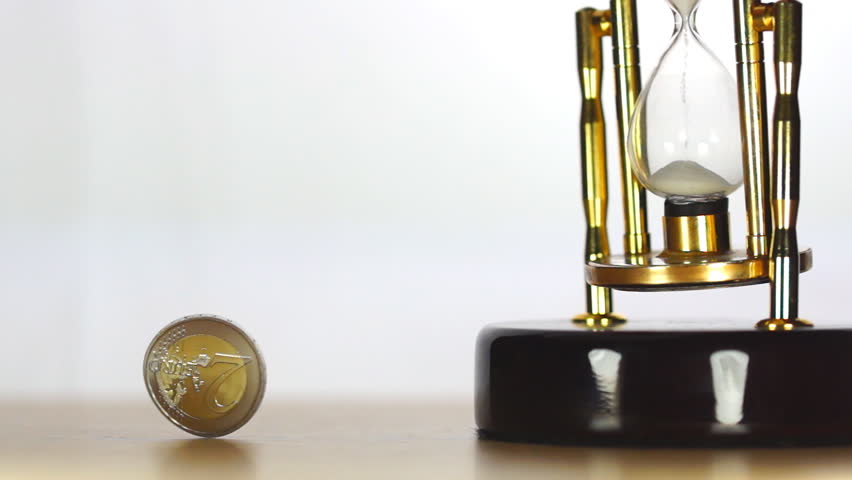Spinning coin near sand clock on the table on white background
