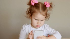 The child is holding a mobile phone, looking at the screen and touches his finger, plays downloaded application on a smart phone close-up.