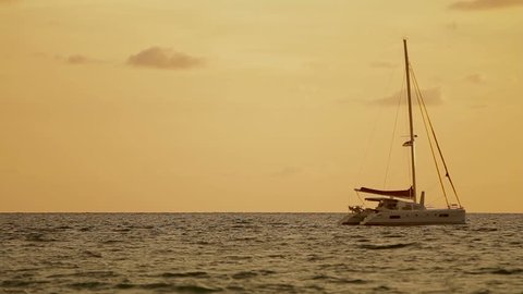 Sunset on Naiharn beach. Sailing yacht sways on the waves. Cloudscape on orange sunset background.
