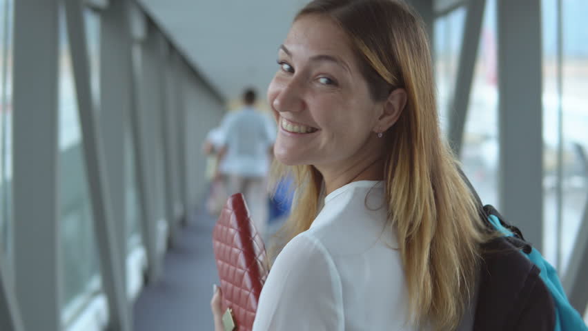 Young handsome woman smiling looking at camera and going to boarding plane at the airport terminal