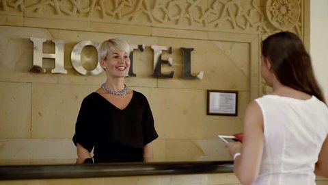 Tourist comes to the reception in the hotel and gives her passport. Receptionist politely checks her passport and gives her the form to fill.