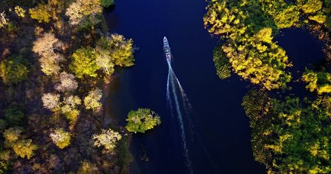 Boat sails in meanders in the river. Aerial image in the Pantanal Biome. Vegetation of riparian forest. Vertical panoramic from the top to the bottom. Mato Grosso do Sul state, Central-Western Brazil.