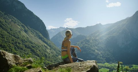 Fit Young Blonde Woman in Sportswear Sits on the Mountain and Drinks Water while Resting. Breathtaking Hills, Mountains, and Valley View. Summer Time with Scenic Nature View. Shot on RED Epic 4K UHD.