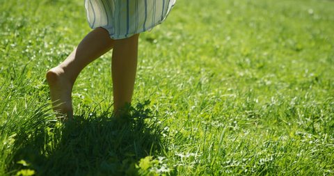 Close-up Shot of the Woman's Legs Walking on the Green Summer Grass. She Wears Stylish Dress. Happy Summer Time. Shot on RED Epic 4K UHD Camera.