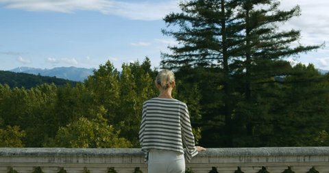 Stylish Young Woman Stands on the Old Town Observation Terrace, Leans on the Balustrade. Beautiful Person with Historic Architecture and Picturesque Nature. Shot on RED Epic 4K UHD Camera.