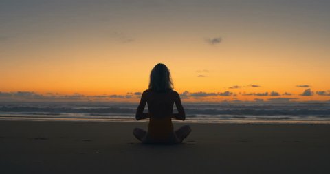 Silhouette of Beautiful Young Woman in the Swimsuit Doing Sitting Yoga on the Beach while Watching the Sunset. Girl Has Blond Hair, is Very Slim and Attractive.  Shot on RED Epic 4K UHD Camera.