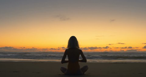 Silhouette of Beautiful Young Woman in the Swimsuit Doing Sitting Yoga on the Beach while Watching the Sunset. Girl Has Blond Hair, is Very Slim and Attractive. Shot on RED Epic 4K UHD Camera.