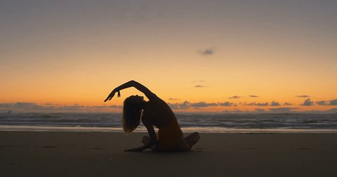 Silhouette of Beautiful Young Woman in the Swimsuit Doing Sitting Yoga on the Beach while Watching the Sunset. Girl Has Blond Hair, is Very Slim and Attractive. Shot on RED Epic 4K UHD Camera.