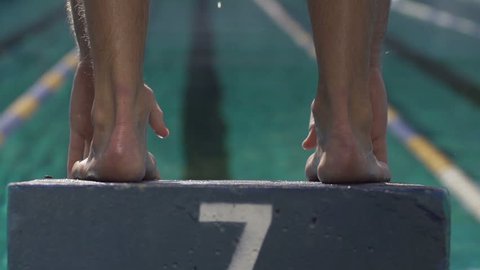 Slow-Motion Shot Of A Professional Male Swimmer Jumping Off The Starting Block Into The Pool.