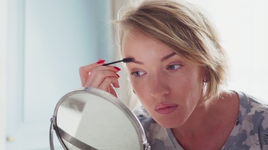 Adult woman doing makeup, corrects eyebrows and looking in the mirror | Shutterstock HD Video #33072790