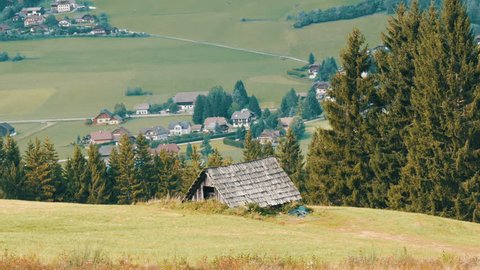 A cozy very old vintage wooden house in the Austrian Alps on a hill with green grass on the background of new modern houses, Old rural country wooden house in village