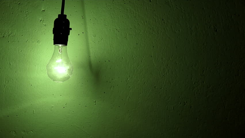 lightbulb swings and flickers against a green textured wall
