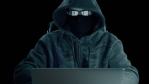 Man in hood sitting at table and coding on laptop. Front view close up. Hacker in balaclava mask and glasses working at computer. Surfing internet man at concrete background. Alpha channel chroma key.