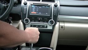 Clip shot from new cars interior with driver using touch screen radio, twisting air on, shifting gears, windshield wipers, to steering wheel for driving.
