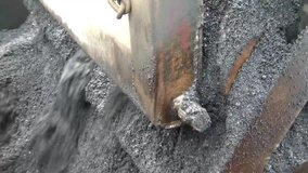 Clip of dumping tar, inner workings of a tar asphalt machine that was churning tar, and moving on a conveyor to ready material for roadwork.