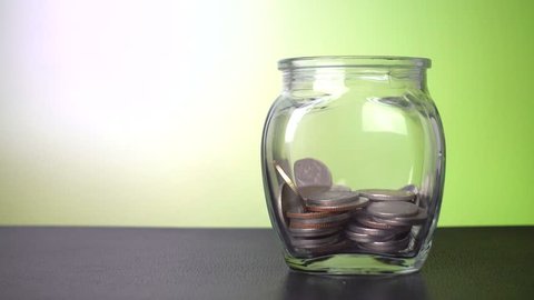 Savings in the jar, coins falling into the jar with green background