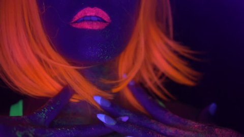 Closeup woman face and body with fluorescent make up in orange wig, creative makeup look great for nightclubs. Halloween party, shows and music concept - slow motion video