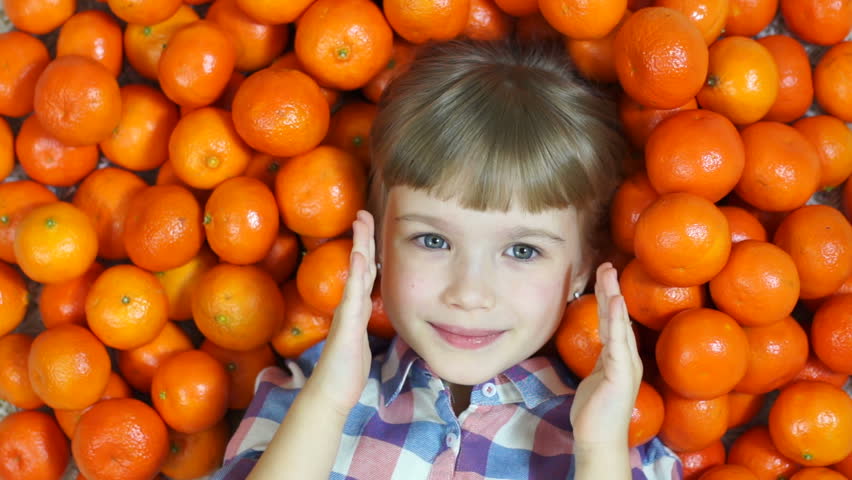 Happy little girl hides in oranges