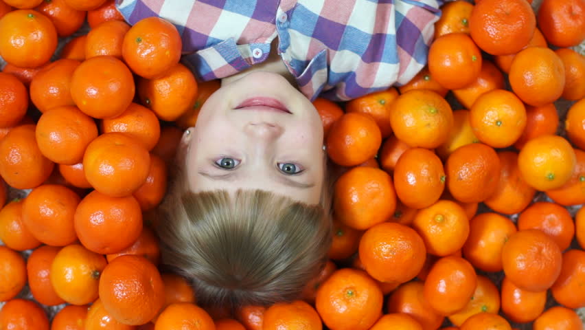 Girl lying in oranges. Looking at camera