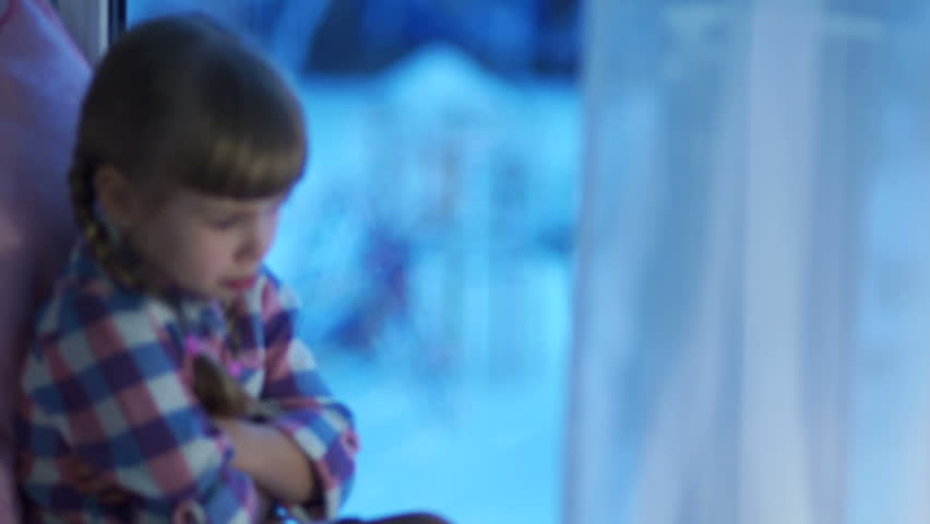 Sad child looking out the window at the snow-covered playground