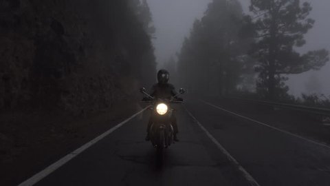 Moto ride in the morning in the woods, fog, mist low visibility rainy ride in the clouds. Scenic oldschool motobike Triumph riding in the mountains.