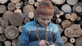 A boy is playing on a smartphone in a village near the wood. Teenager on the farm playing on the smartphone in the game 4K video.