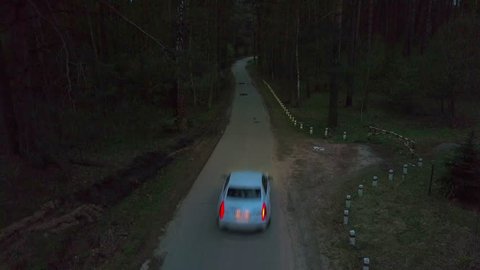 White Cadillac Cts car driving along the road in the autumn night forest. Aerial rear landing view
