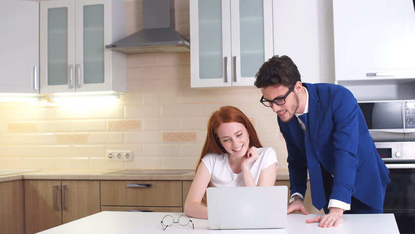 Happy business couple looking at laptop at home in kitchen.