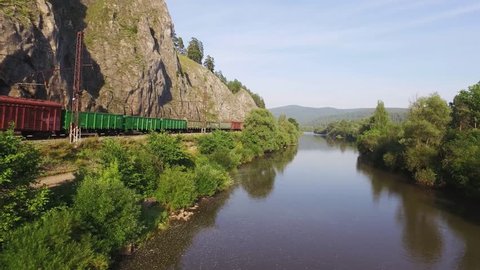 Freight train carries an electric locomotive by two-sided railway along the river in the Ural Mountains - Aerial Photography, top view