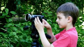 Young boy looks into video camera on background of green park. Children outdoors in summer are creative work of cinema. Beautiful footage for family. Interesting world in childhood.