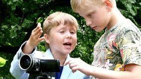 Young boys with video camera shoots film about nature of green park background. Children outdoors in summer are creative work of cinema. Beautiful footage. Interesting to look at world in childhood.