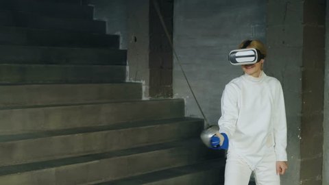 Concentrated fencer woman using virtual reality headset for play fencing training simulator game indoors