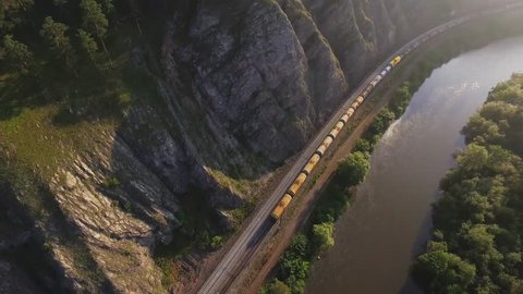 Freight train carries with oil tank an electric locomotive by two-sided Trans Siberian railway along the river in the Ural Mountains - Aerial Photography, top view