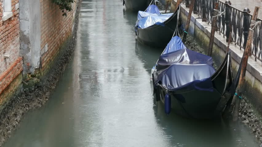 VENICE, ITALY, SEPTEMBER 7, 2017: Venetian gondolas stand on the canal in the rain, Beautiful black gondolas stand and rock on the waves