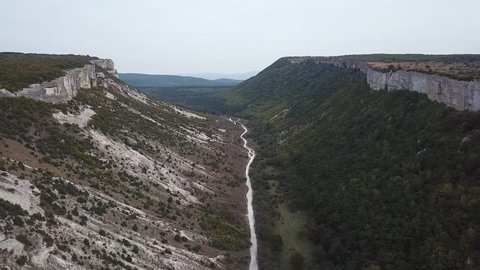 Aerial View: a span in the middle of a canyon, on one side of the cliff, on the other side of the forest. In the middle of the river flows. Crimea, Mangoop in 4K