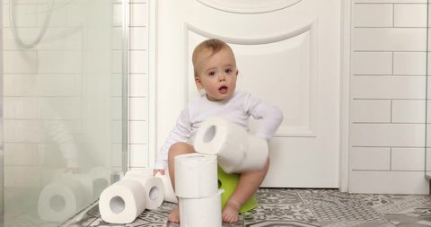 Funny baby boy sitting on chamberpot, Children's legs hanging down from a chamber-pot. Kid plays toilet paper