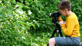 Young boy with video camera shoots film about nature of green park background. Children outdoors in summer are creative work of cinema. Beautiful footage. Interesting to look at world in childhood.