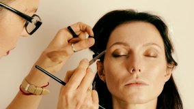 Make-up artist applying eyes make-up to an adult woman model - close-up 4k video