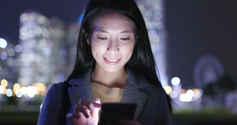 Woman looks at mobile phone in city at night
