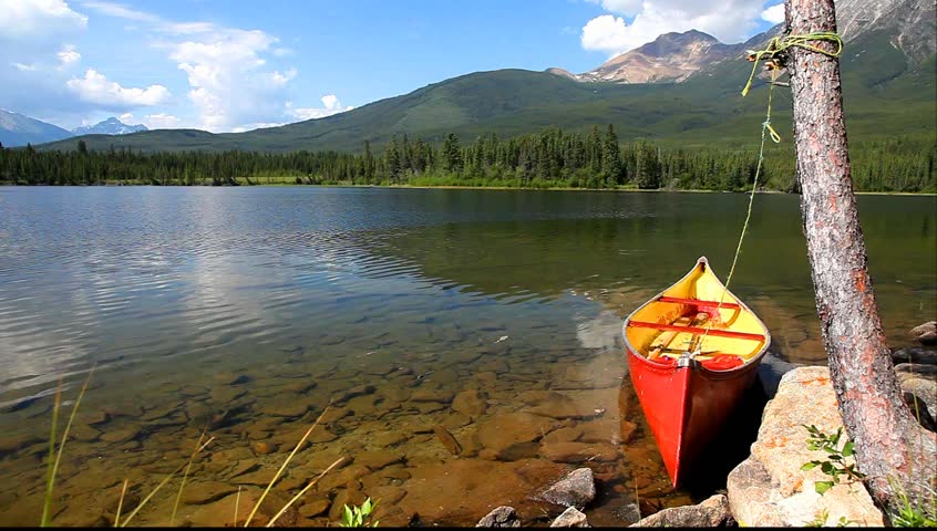 Old red canoe adhered to a tree on fine lake in an environment of mountains (Maligne Lake. Jasper National Park, Alberta, Canada) 