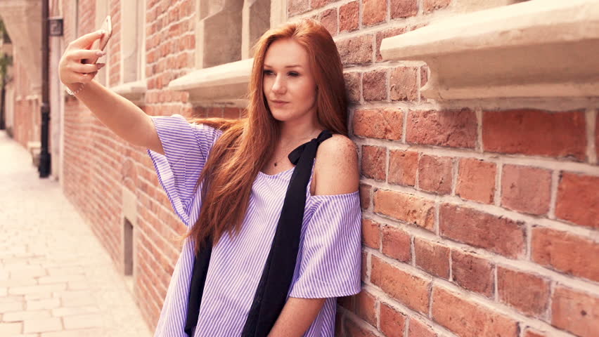 Young, pretty woman taking selfie photo standing by the wall in the city
