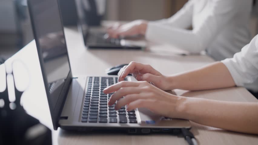 A close shot at the hands of a woman who quickly prints text on the laptop keyboard, the ladies are working in the office behind a portable device | Shutterstock HD Video #33134923