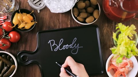 Time lapse. Writing sign for Bloody Mary bar on black cutting board. Olives, pickles, celery, and cocktail shrimp to garnish bloody mary cocktail.