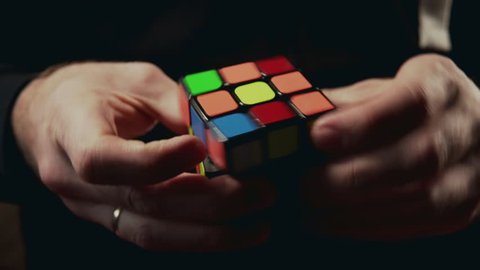 Minsk, Belarus - NOVEMBER 20, 2017: Boys hands solving Rubik's Cube 3x3x3 at dark background. Rubics cube is the world's top-selling puzzle game and one of the world's best-selling toys in 4k