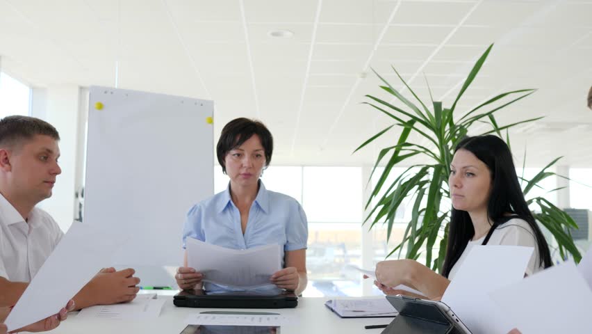 Business meeting of collaborators at desk with documents in hand in boardroom with large windows | Shutterstock HD Video #33145957