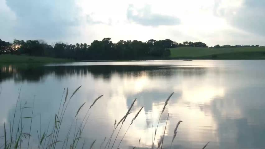 Image of pretty lake in beginning, then camera is lifted into frame and hands snap two pictures.