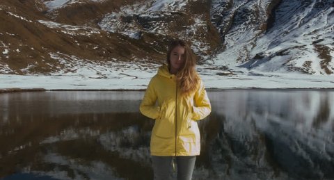Young female hiker standing near peaceful mountain lake, looking into camera. French Alps, Sixt-Passy nature preserve, Lac d’Anterne.  4K UHD 60 FPS SLO MO