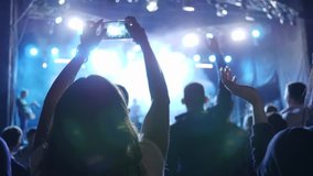 smartphone in arms of fan makes video on background dancing crowd at youth event in night