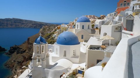 Panning view of white houses and blue dome churches on the steep cliff in Santorini Island, Greece. Aegean Sea