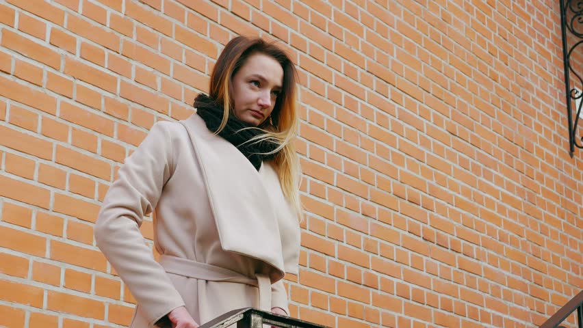 Beautiful young girl with an attractive appearance, adorable look, scarf and autumn coat in the city. Amazing view of business lady walking down the city street.